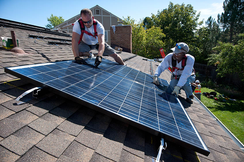 Two workers install a solar panel on the roof of a house.