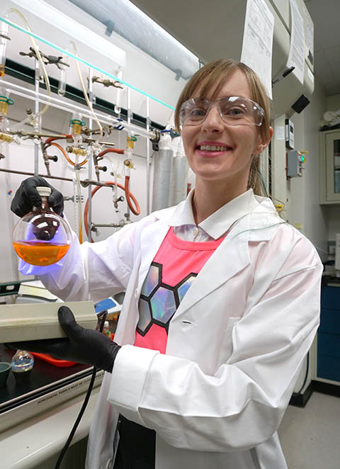 A photo of a researcher in a lab holding a beaker of orange fluorescent liquid