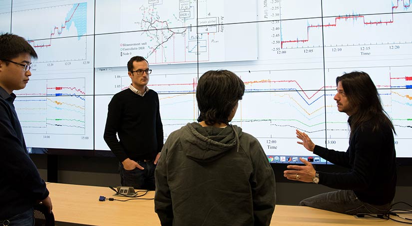Andrey Bernstein talks with fellow researchers about data showing on a large screen.