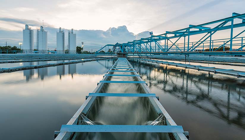 Photo of a wastewater treatment facility with water in the foreground and filters from the foreground to the background that has a water pumping station