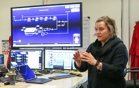 A researcher speaks in front of a monitor showing a research diagram.