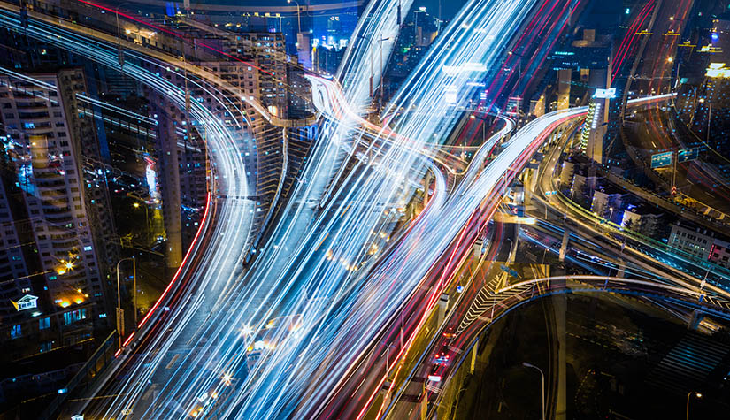 An aerial time-lapse photo of a nightime cityscape with traffic shown in streaks of light