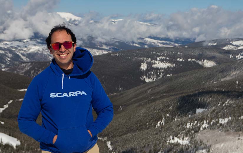 Photo of Tarek Elgindy standing on top of a mountain with more mountains in the background.