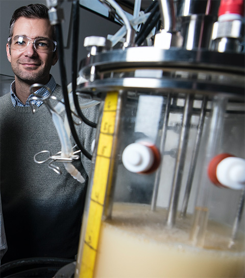 A man stands next to lab equipment containing a microbe.