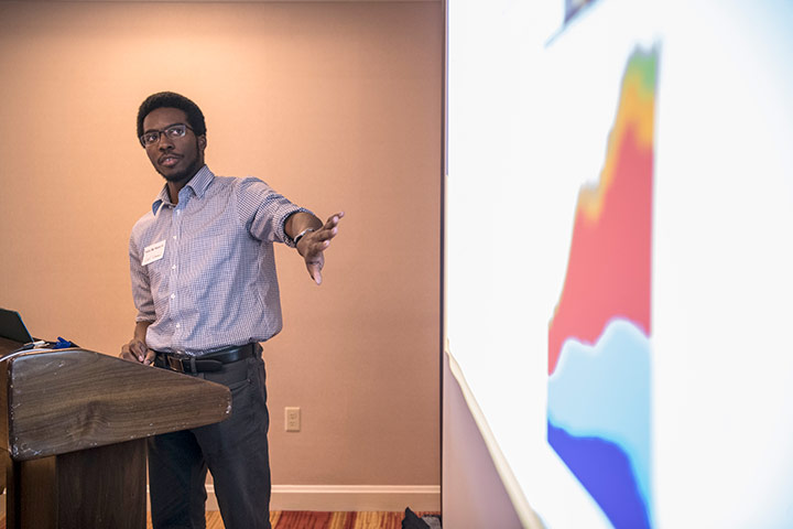 Student at lectern pointing to a presentation slide projected on the wall.