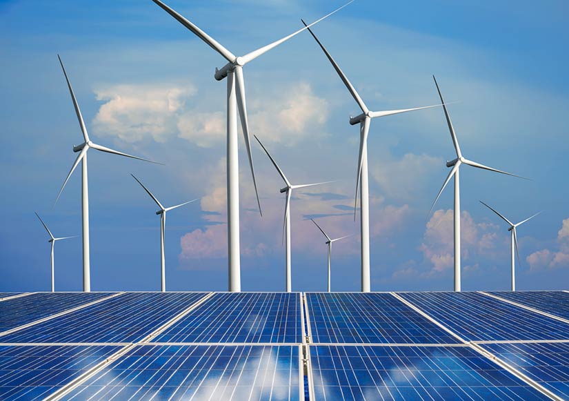 Photo of solar panels in the foreground and wind turbines in the background.