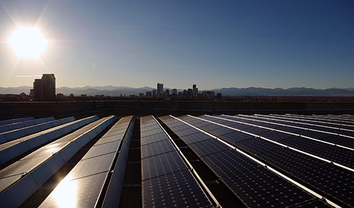 Photo of solar panels on a rooftop with a city skyline and mountains in the background.