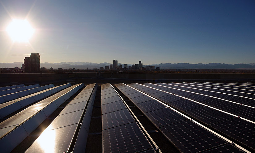 Photo of solar panels on a rooftop with a city skyline and mountains in the background.