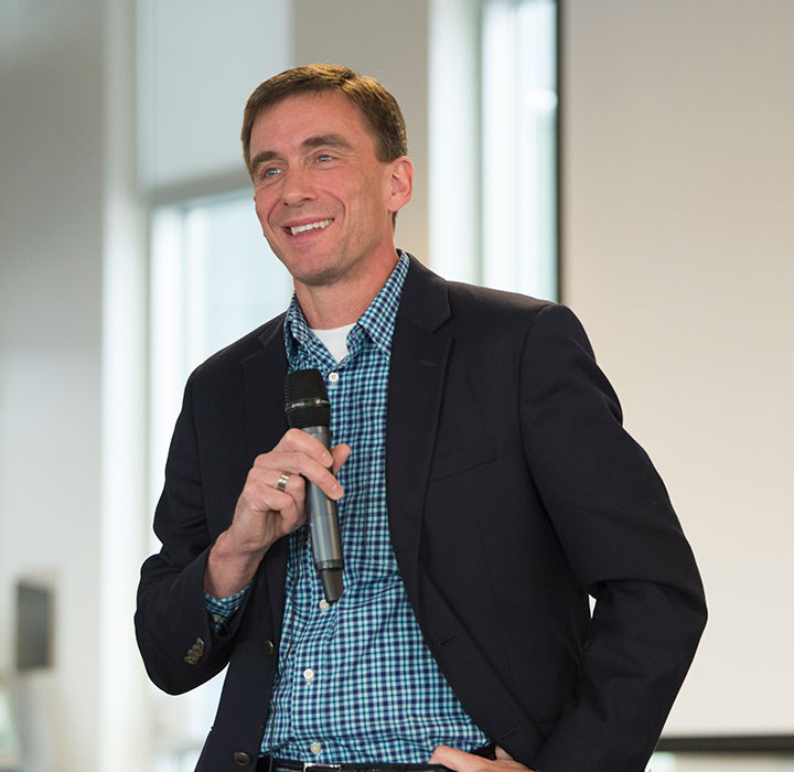 A man smiles as he speaks into a microphone.