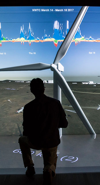 A man crouches looking at a visualization of a wind turbine. 
