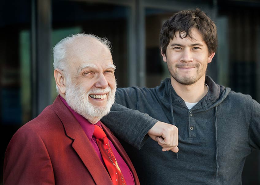 A smiling man in a red suit stands with one of his students.