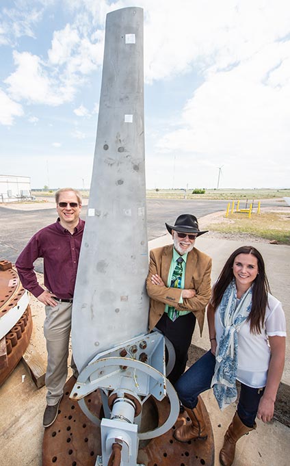 Photograph of three people standing next to a water blade in an open field. 