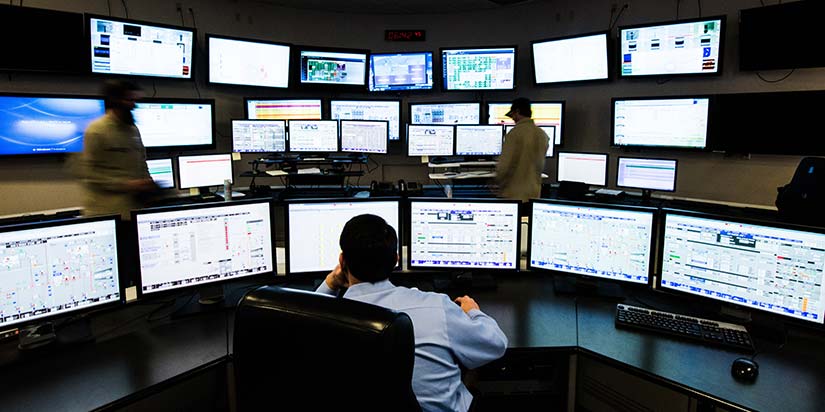 Man sitting at desk with multiple computer screens in front of him.