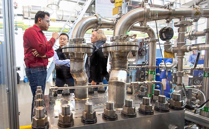 Three researchers stand behind an electrolyzer.