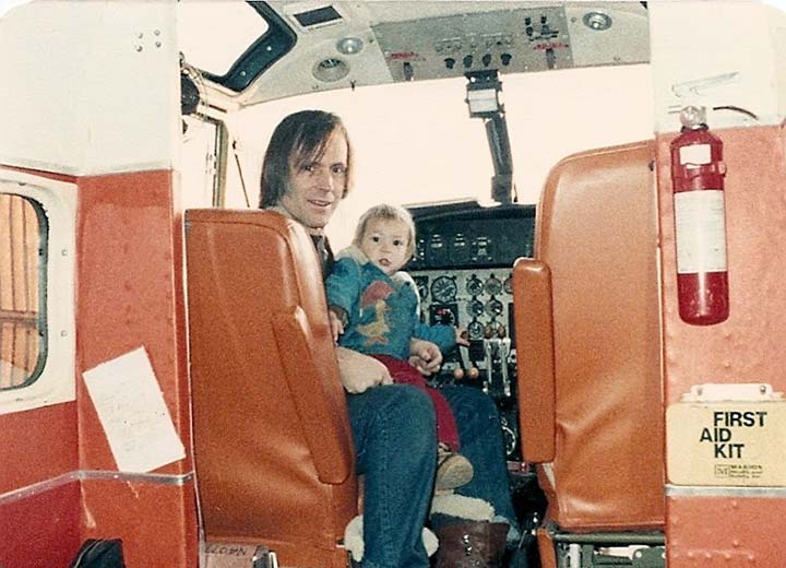 A child sitting on a man's lap in the cockpit of an airplane.