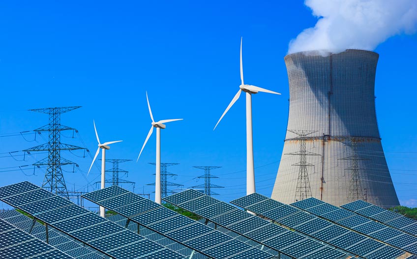 Photo of diverse energy sources, including solar panels in the foreground with a nuclear reactor, wind turbines, and power lines in the background.