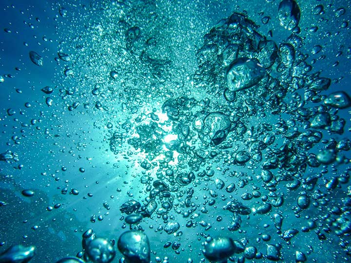 Bubbles in green-blue ocean water, light shining through them from behind.