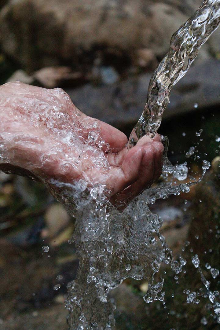 Photo of a hand outstretched to catch a stream of water.