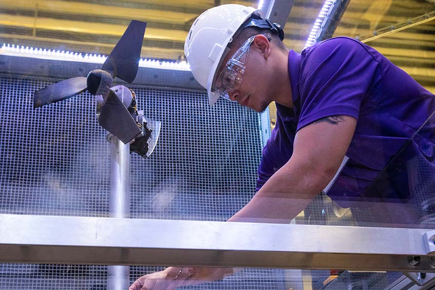 A student prepares a wind turbine inside a wind tunnel. 