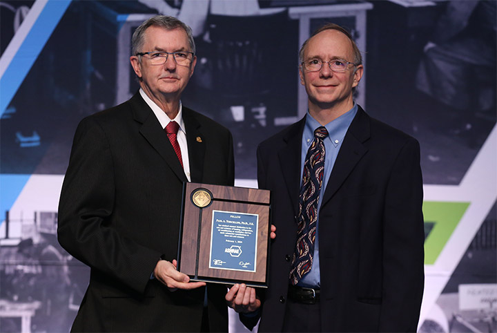 Two people stand holding a plaque on stage.