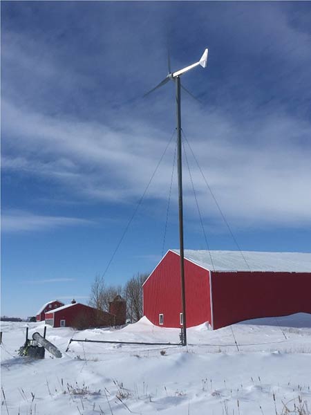 A photograph of a red barn with a small, distributed wind turbine in the foreground.