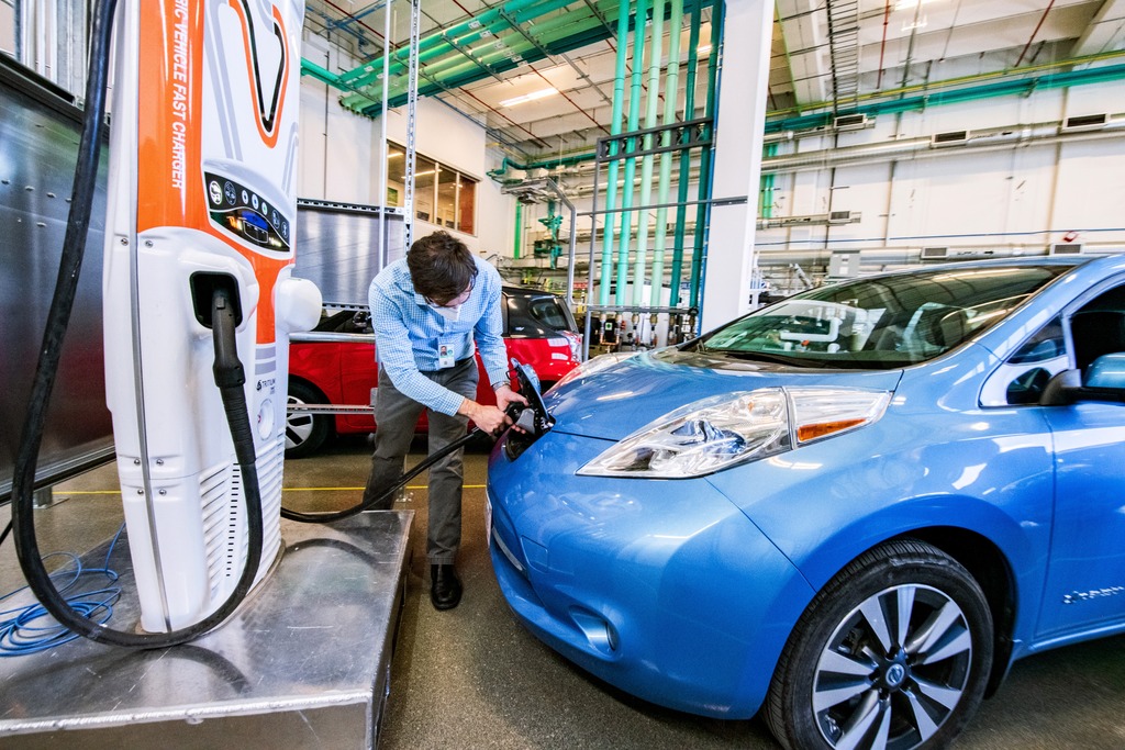 An NREL researcher plugs a blue electric car into a charging port. 