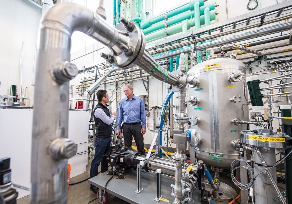 Two people stand behind an electrolyzer. 