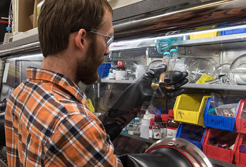 A man in a lab holds up three vials. 