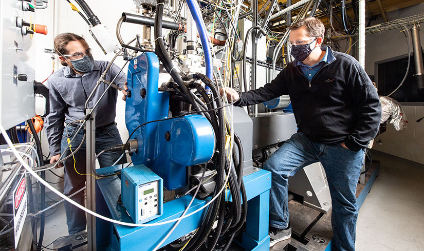 Photo of two researchers working with an advanced fuels test engine in a lab