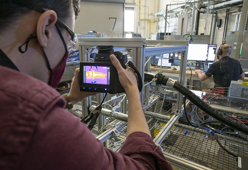 Photo of a reseacher using a thermal camera to image electric vehicle charging equipment in a lab