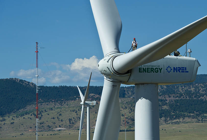 Man standing on wind turbine in a harness and hard hat