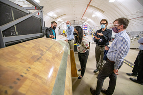 A group of people stand around a wind turbine blade inside a hangar