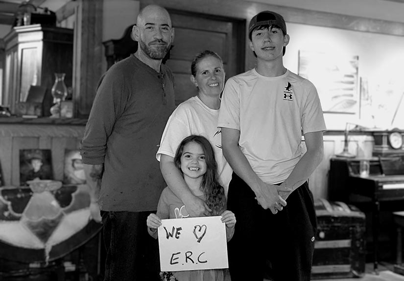 A black and white photo of a family standing in their home holding an I love ERC sign.