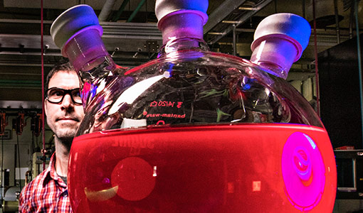 Photo of a researcher standing behind a large beaker filled with red liquid