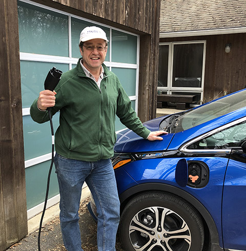 Photo of a man standing next to an electric vehicle and about to plug in the car's charging cable