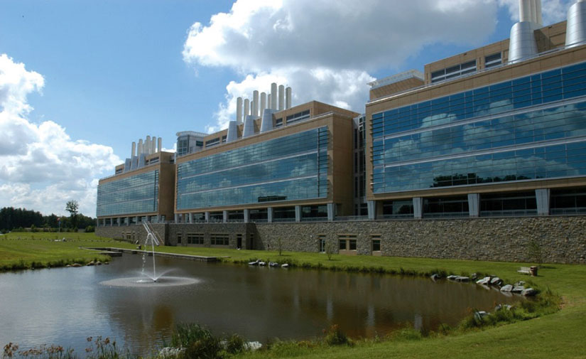 Photo of a large building with blue sky and a pond with fountain in the foreground