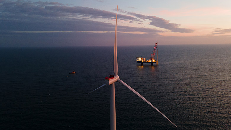 A wind turbine installation vessel floats beside an offshore wind turbine.