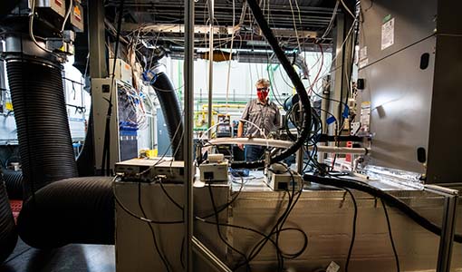 Photo of a man standing in a lab behind wires and tubes that are part of an indoor state-of-the-art heat pump attached to the ventilation system.