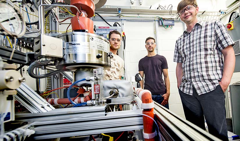 Three people stand in a laboratory with machinery.