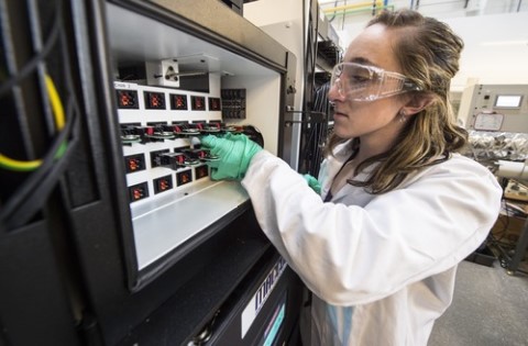 Photo of Kae Fink wearing a white lab coat and green gloves. She is handling samples. 