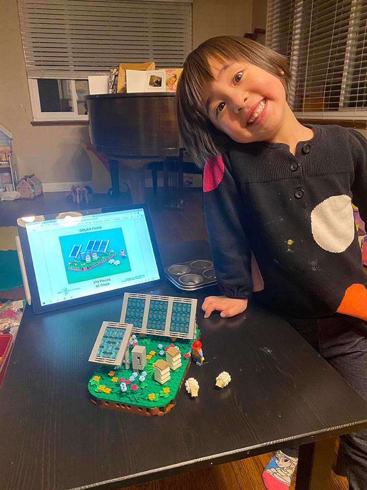 A child smiling with a constructed Lego solar farm kit prototype.
