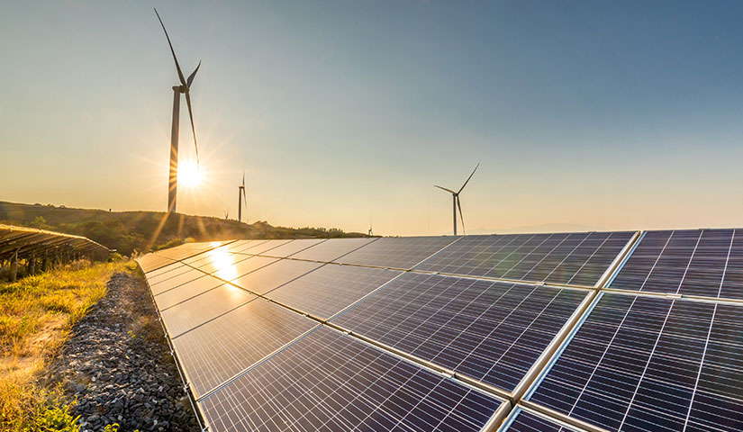 Photo of solar panels in the foreground and wind turbines in the background.