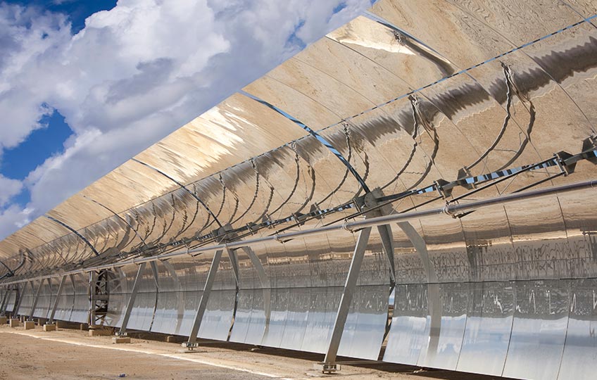 Photo close-up of a solar trough collector, or a solar panel that is curved in a parabola shape and lined with a polished metal mirror. Blue sky and clouds are in the background.