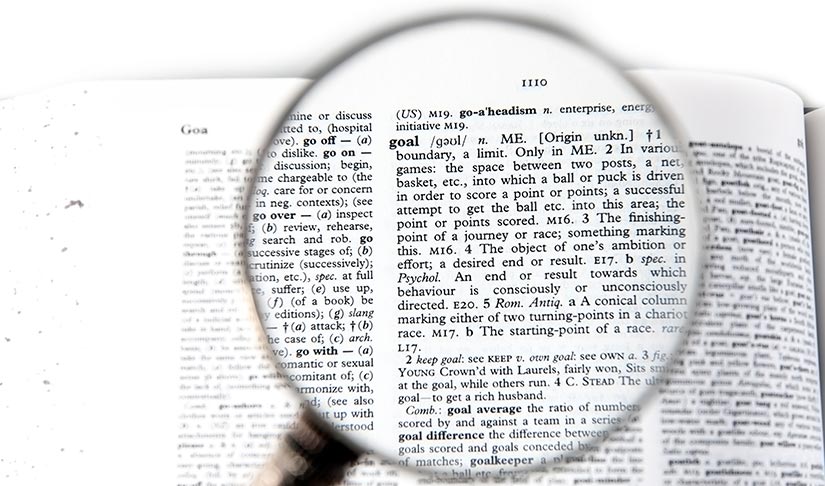 Photo of a magnifying glass hovering over a page in the dictionary. 