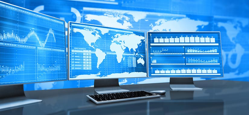 A stock image of three desktop monitors with maps and charts displaying on the screens.