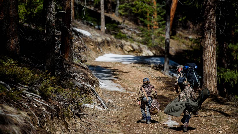 Photo of a father and his two sons walking on a trail outside. They have heavy packs for a hunting trip.