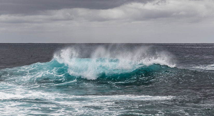 Turquoise wave crashing, surrounded by grey waters and a stormy sky.