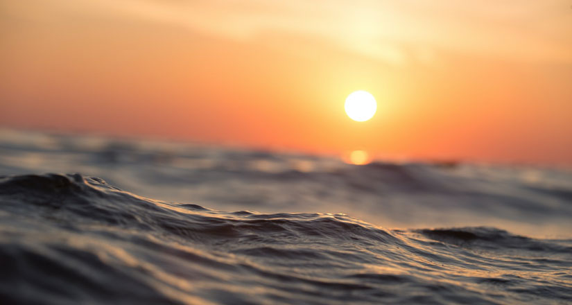 Image of ocean waves, an orange-red sky and yellow sun are in the background.