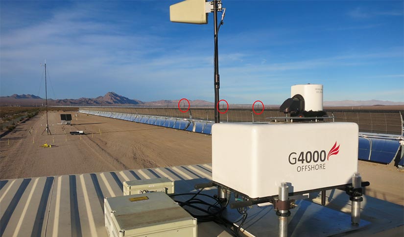 A box-shaped device next to a row of solar devices in a desert