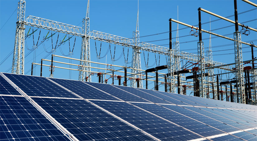Image of a group of solar panels with electric generation and distribution power lines behind them.